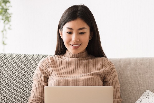 Woman On Sofa Smiling Looking At Laptop